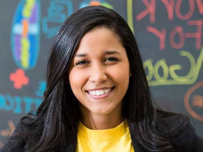 Woman dressed business like smiling for a picture infront of a colorful chalk board